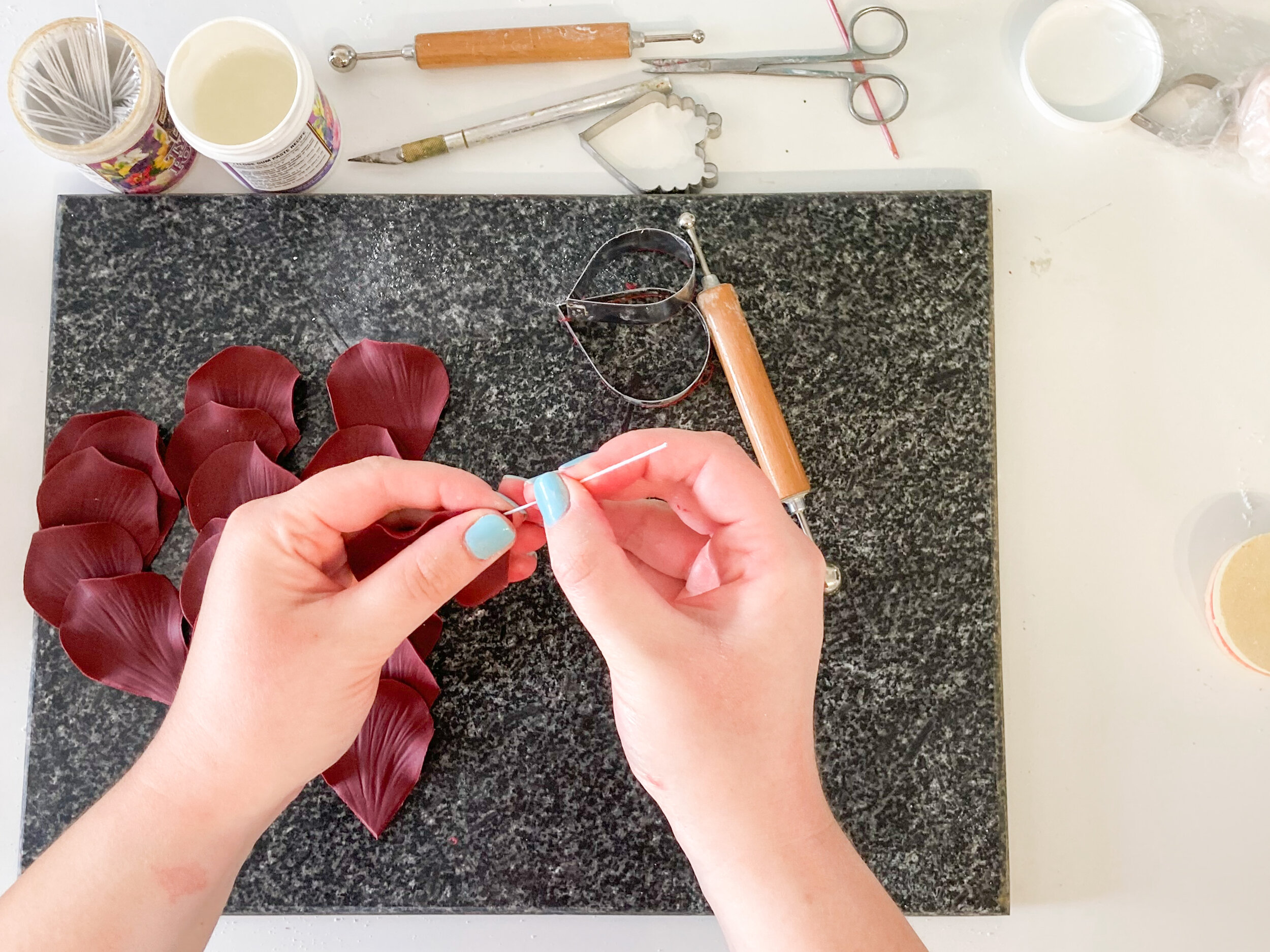A woman making burgundy flower petals on a granite cutting board. 