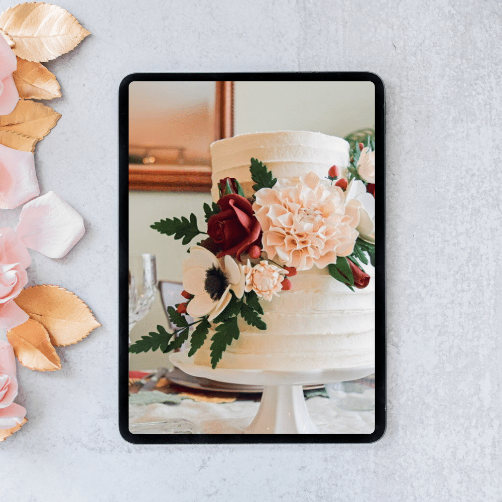 ipad on a gray surface showing a photo of a two tier cake with sugar flowers