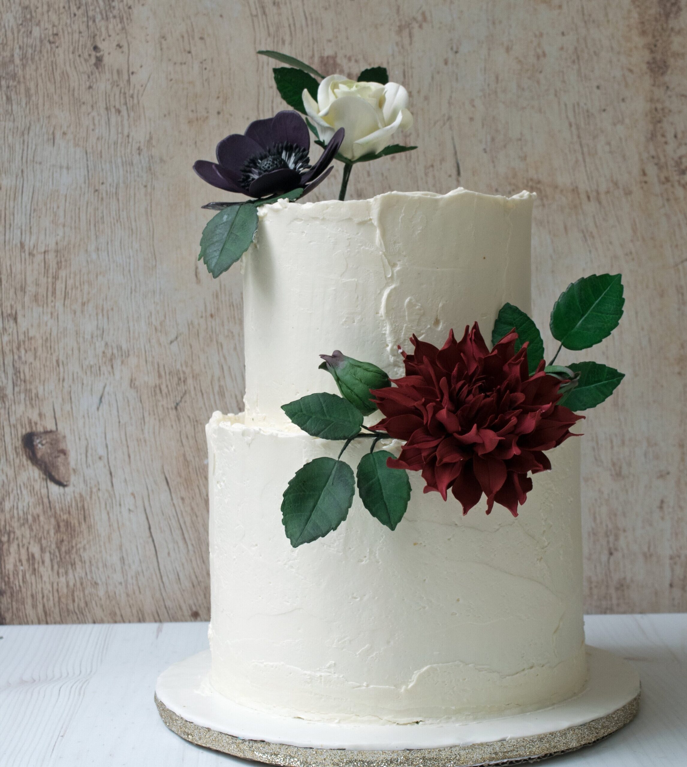 two tier cake decorated with burgundy dalia, purple anemone, and white rose as an alternative to using fresh flowers for cakes