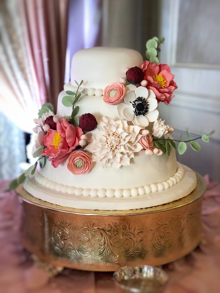 Sugar Flower Cascade including 3 large flowers, 2 medium flowers, 3 small flowers, assorted leaves buds and berries on a 3 tier cake. Includes dusty pink peonies, anemones, pink ranunculus, and ivory dahlias.