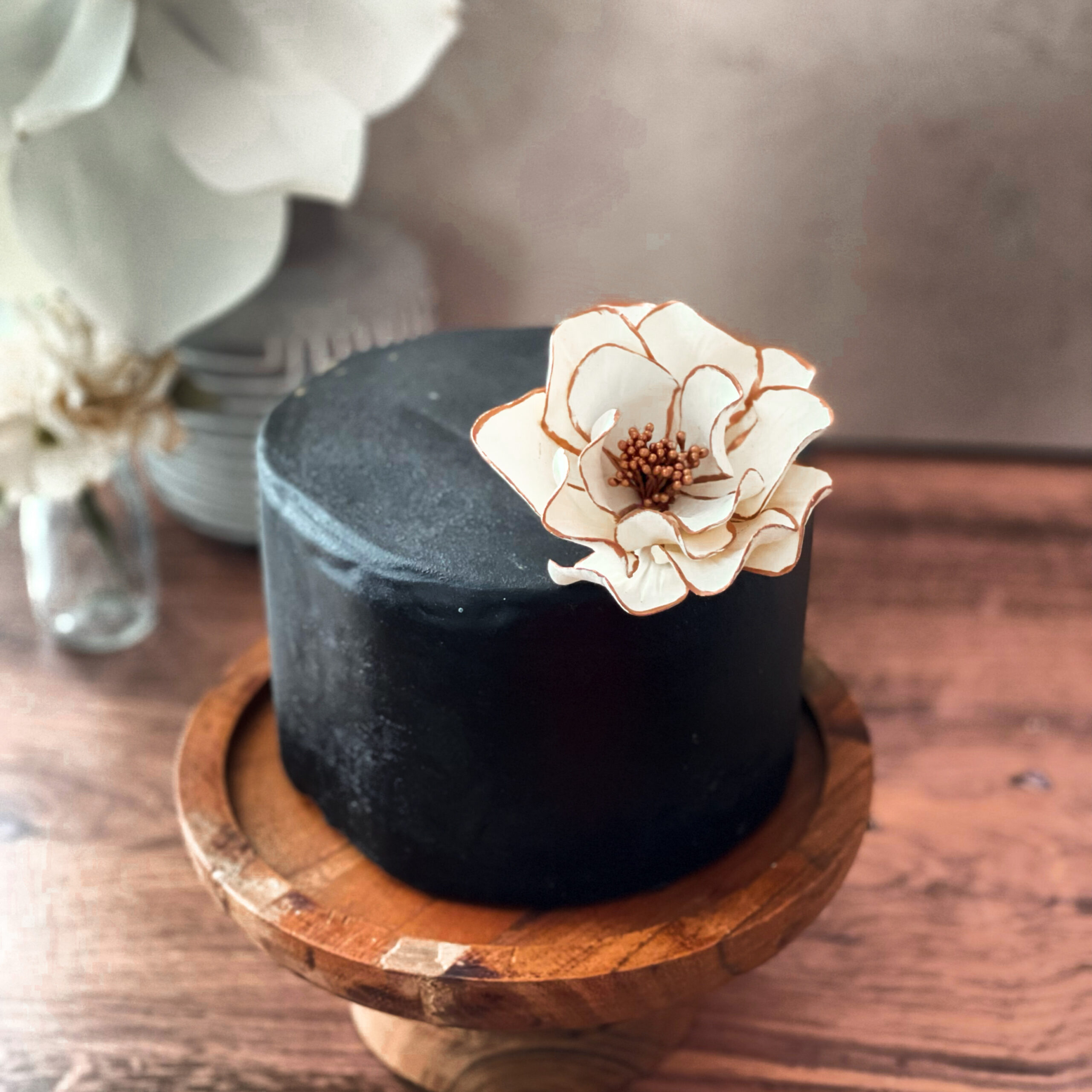 white open rose with rose gold edging displayed on a one tier cake covered in black fondant