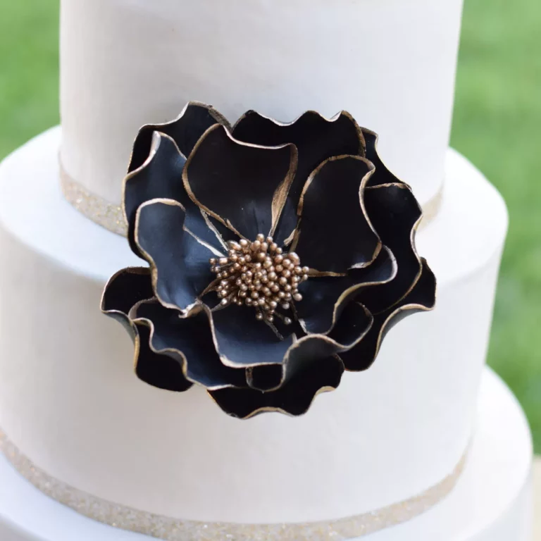 extra large black and gold edged open rose sugar flower on a two tier white fondant wedding cake