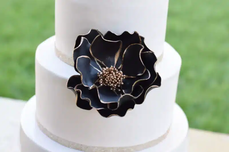 extra large black and gold edged open rose sugar flower on a two tier white fondant wedding cake