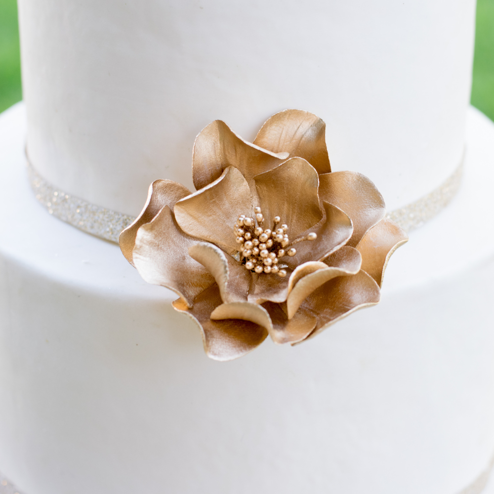 small gold open rose sugar flower close up on a two tier cake