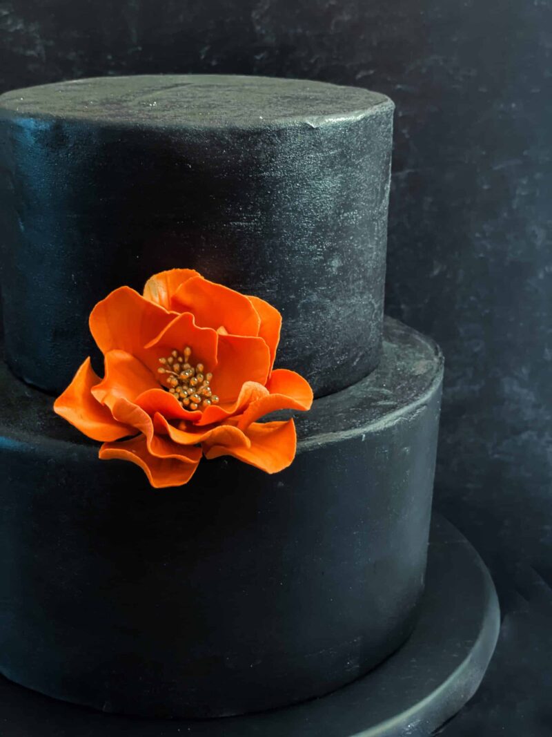 Small open rose terra cotta burnt orange and gold On a black cake