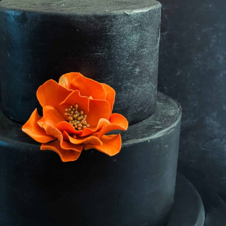 Small open rose terra cotta burnt orange and gold On a black cake