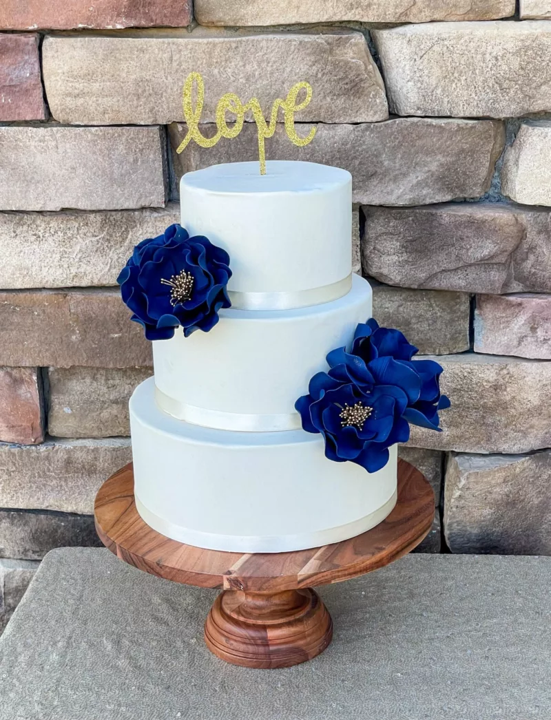 Set of four navy open roses on a three tier cake with gold stamen centers