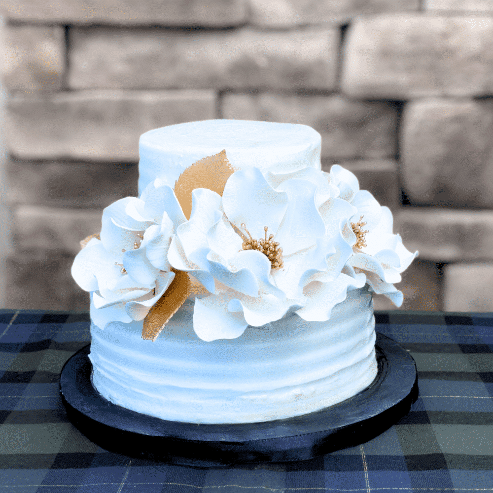 three white and gold open rose sugar flowers on a two tier white buttercream cake