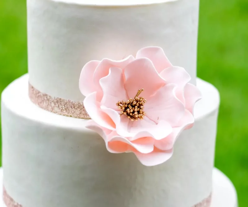 large blush gold open rose sugar flower on a two tier white fondant wedding cake