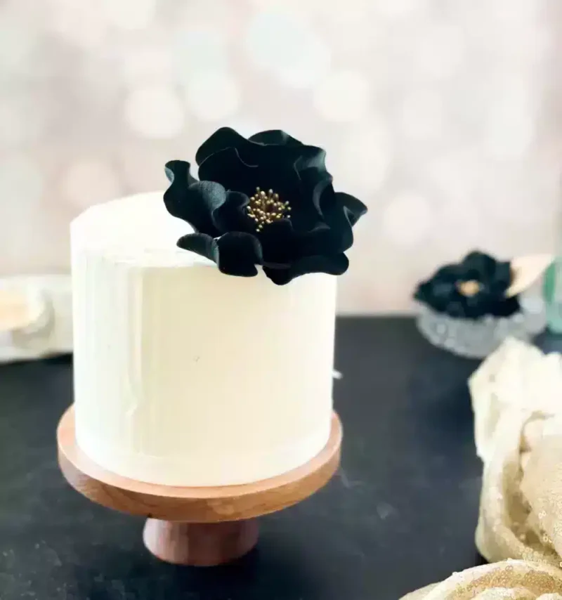large black and gold open rose sugar flower decorating a small buttercream cake