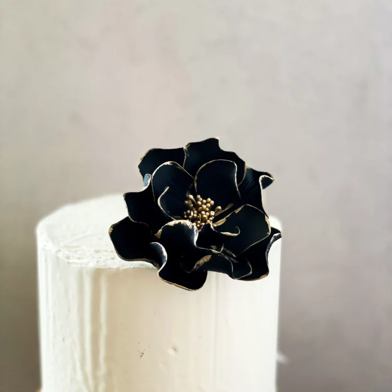 medium black and gold edged open rose gumpaste flower on a small buttercream cake