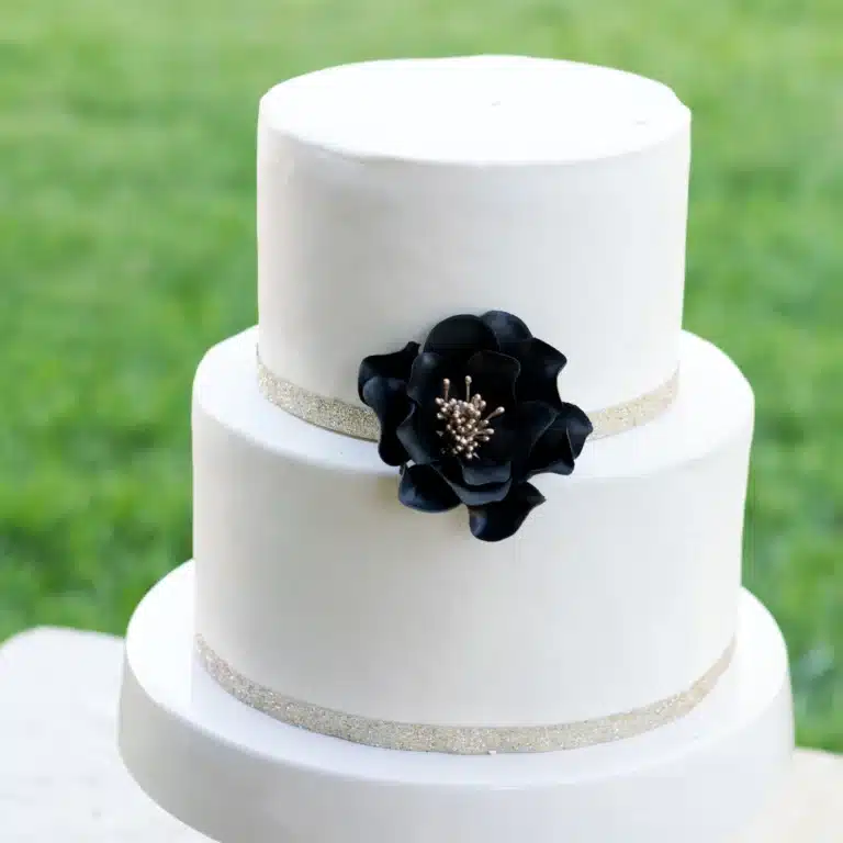 small black and gold open rose sugar flower on a two tier white fondant wedding cake