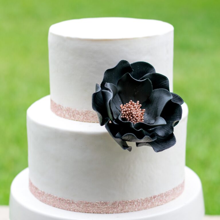 extra large black and rose gold open rose sugar flower on a two tier white fondant cake