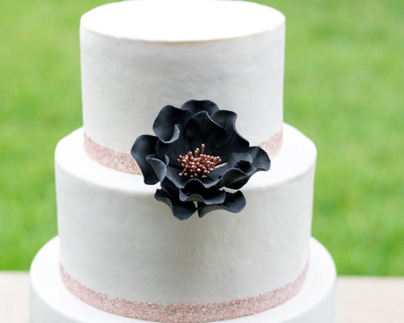 medium black and rose gold open rose sugar flower on a white two tier fondant cake