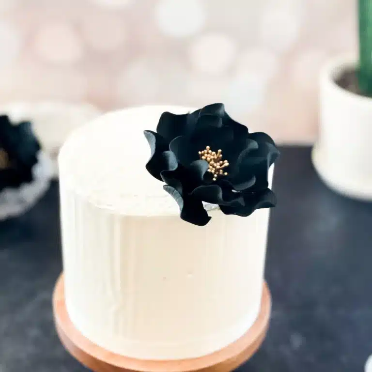medium black and gold open rose gumpaste flower on a small buttercream cake