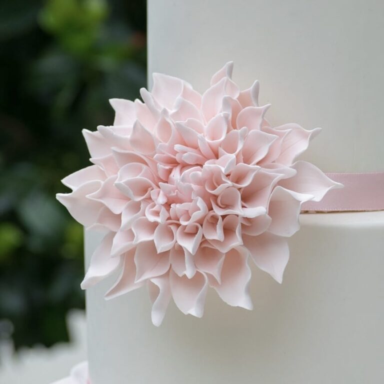 Large blush dahlia sugar flower on a two tier white fondant wedding cake
