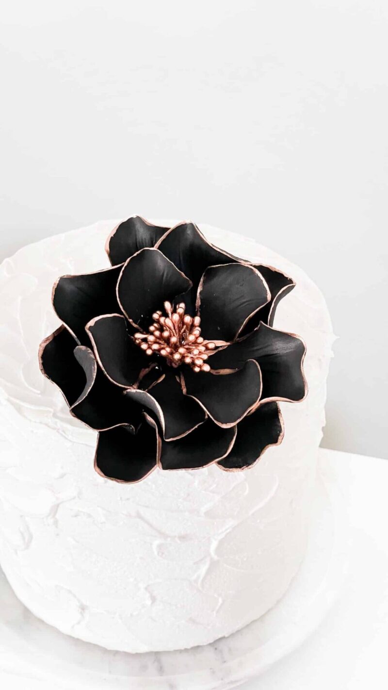 black and rose gold edged open rose Gumpaste flower on a small white buttercream cake