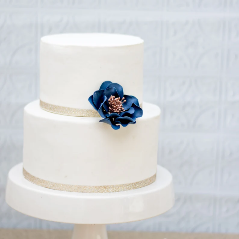 Small navy and rose gold open rose gumpaste flower decorating a white fondant two tier cake