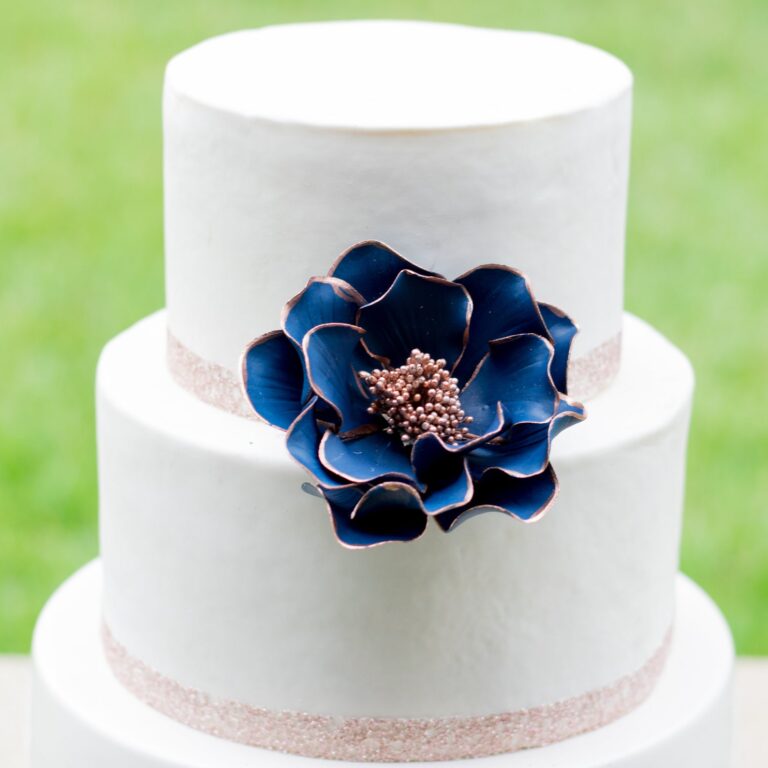 Large Navy and rose gold edged open rose sugar flower displayed on a white two tier fondant cake