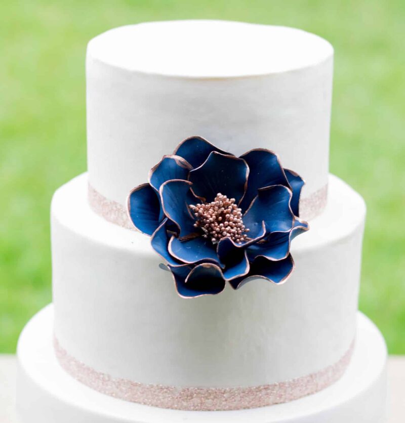 Large Navy and rose gold edged open rose sugar flower displayed on a white two tier fondant cake