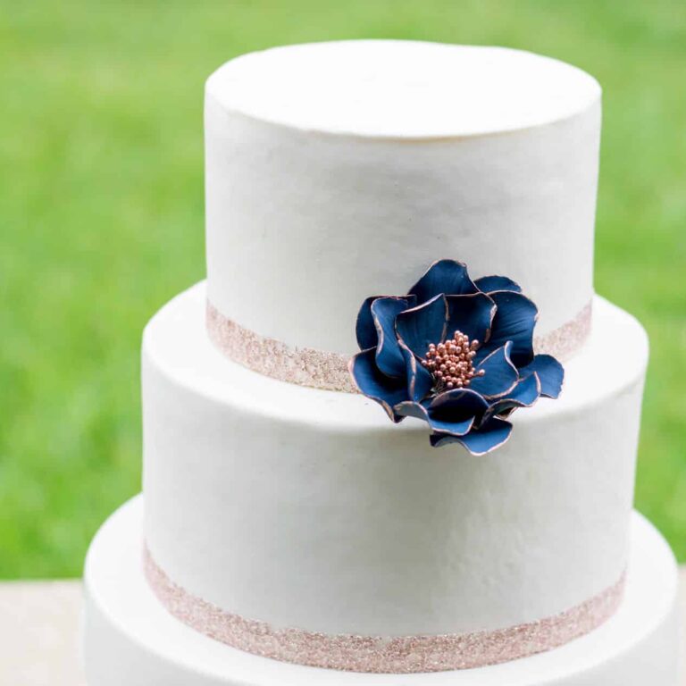 Navy and rose gold edged open rose sugar flower displayed on a white fondant two tier cake
