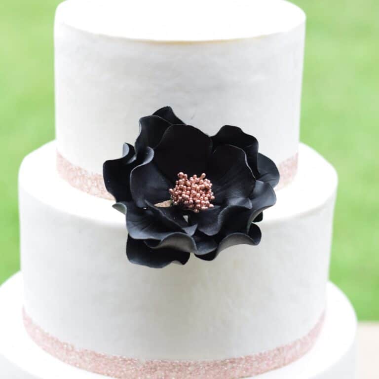 large black + rose gold open rose sugar flower on a two tier white fondant wedding cake