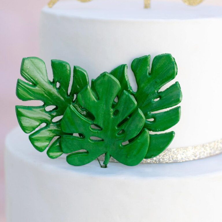 A close up of three small vibrant green monstera leaves arranged in a cluster on a white cake