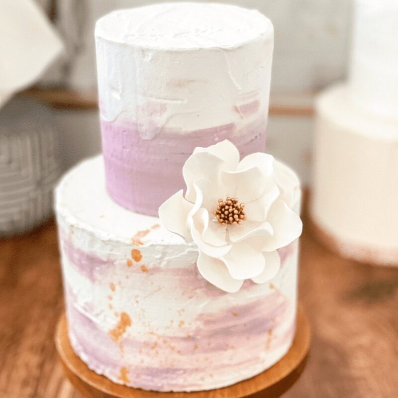 small white gold open rose sugar flower decorating a two tier purple buttercream cake