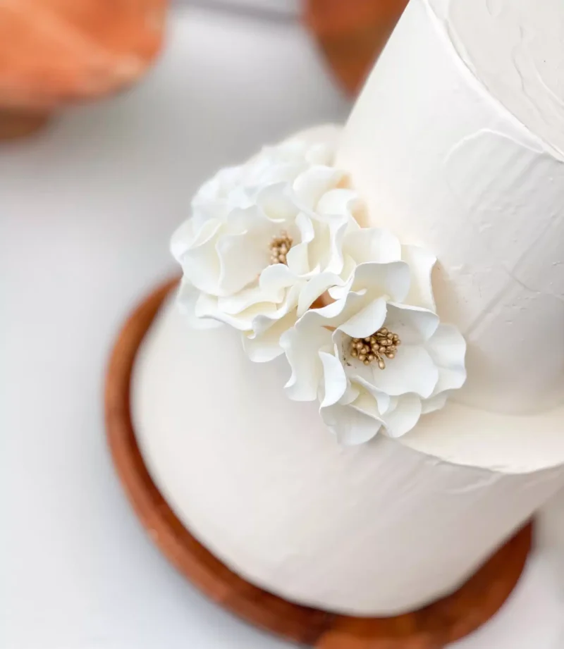 three small white and gold open rose sugar flowers on a two tier white fondant wedding cake