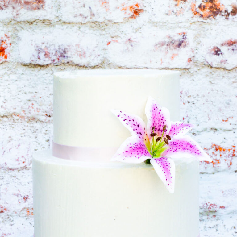 pink and white stargazer lily sugar flower sitting on a white two tier buttercream cake