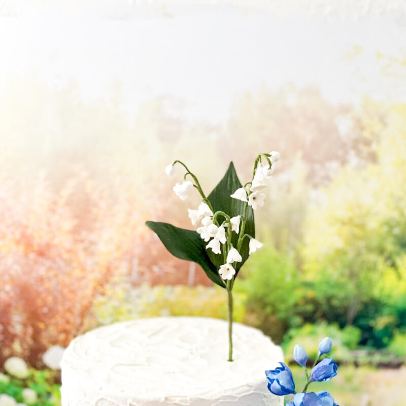 A white and green lily of the valley sugar flower on top of a white cake.