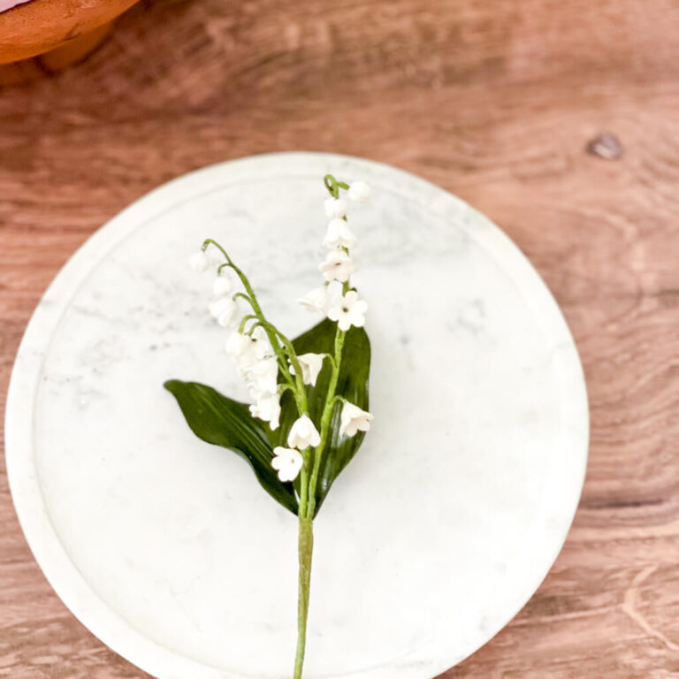 Elegant white lily of the valley sugar flower on marble cake stand, against wooden table